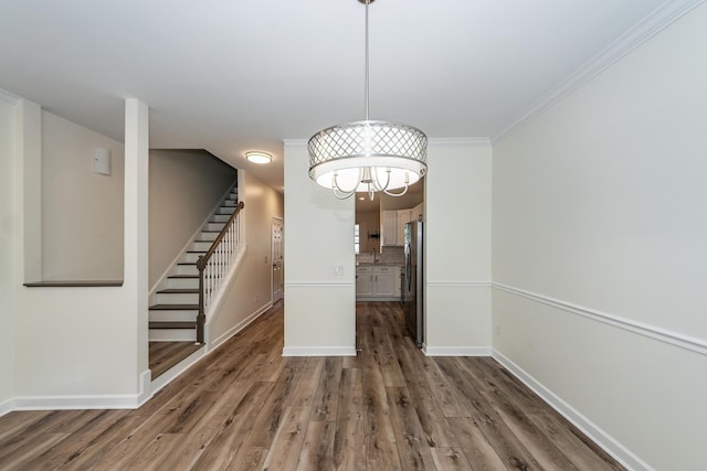 unfurnished dining area featuring stairway, dark wood-type flooring, baseboards, a chandelier, and crown molding