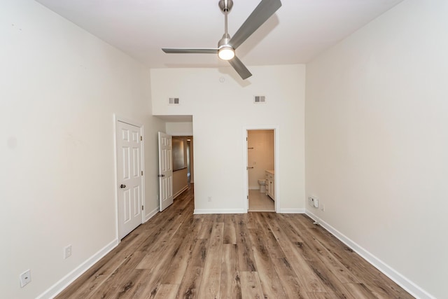 unfurnished bedroom featuring high vaulted ceiling, wood finished floors, baseboards, and ensuite bathroom