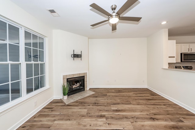 unfurnished living room featuring ceiling fan, wood finished floors, recessed lighting, a tiled fireplace, and baseboards