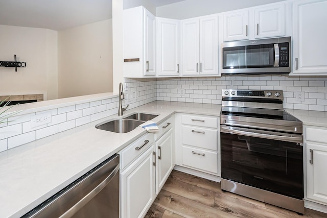 kitchen with appliances with stainless steel finishes, a sink, wood finished floors, light countertops, and white cabinets