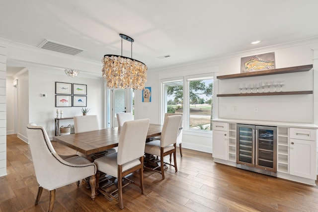 dining area featuring ornamental molding, indoor bar, wood-type flooring, and beverage cooler