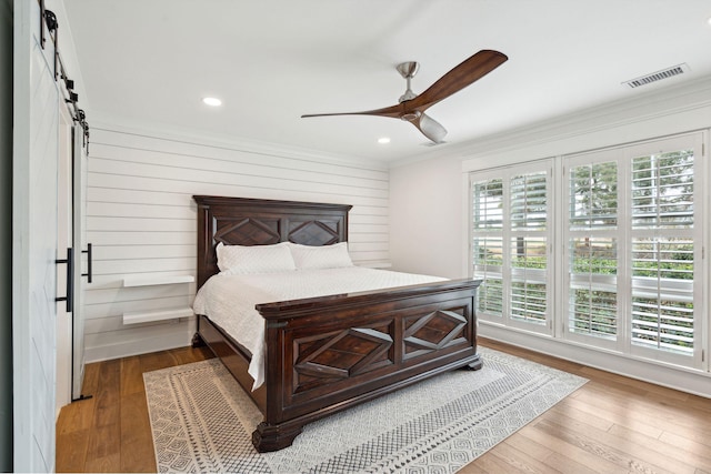 bedroom with crown molding, wood-type flooring, a barn door, and ceiling fan