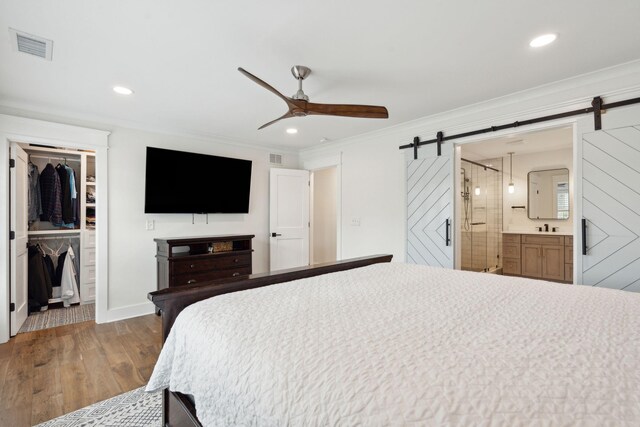 bedroom featuring crown molding, wood-type flooring, a barn door, a spacious closet, and a closet