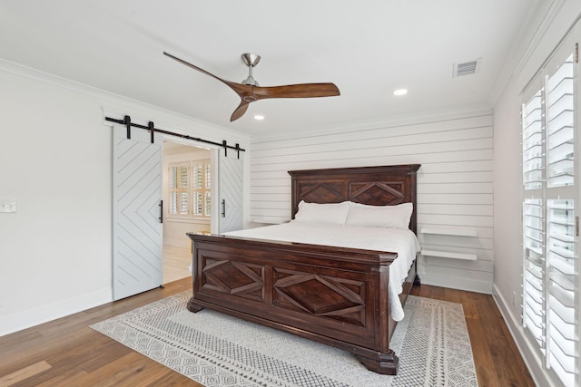 bedroom featuring dark hardwood / wood-style floors, ceiling fan, ornamental molding, and a barn door