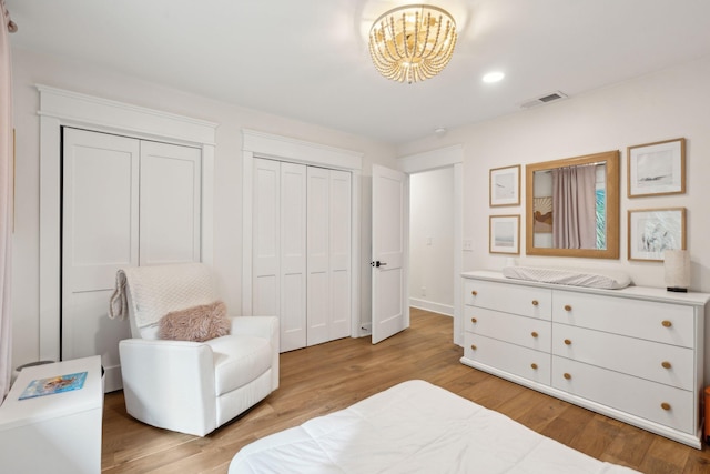 bedroom with multiple closets, light hardwood / wood-style floors, and a notable chandelier