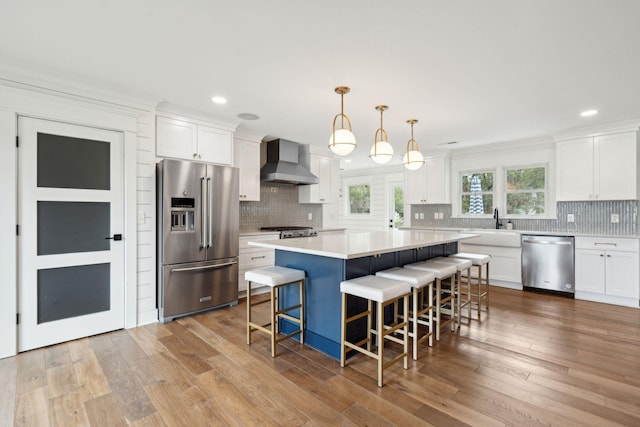 kitchen with white cabinetry, appliances with stainless steel finishes, hanging light fixtures, and wall chimney range hood