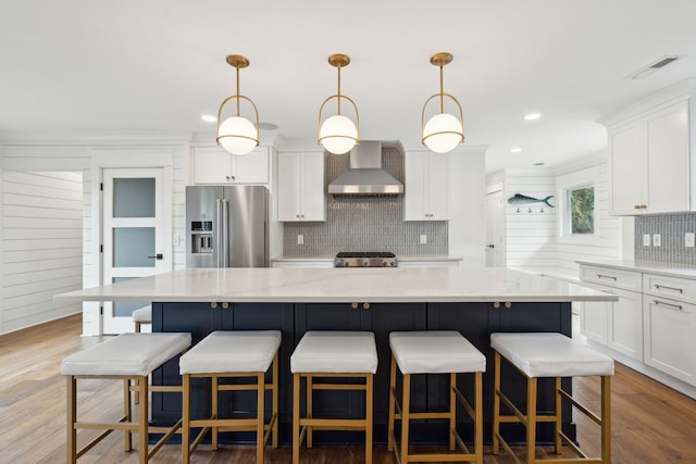 kitchen with a spacious island, wall chimney exhaust hood, high end fridge, and pendant lighting