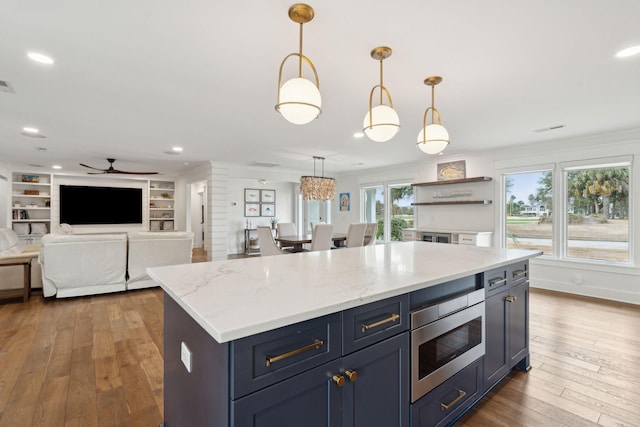 kitchen featuring pendant lighting, stainless steel microwave, a center island, light stone countertops, and dark wood-type flooring