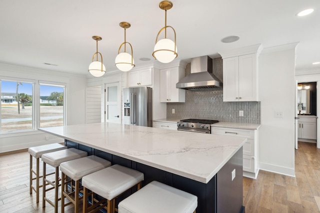 kitchen featuring pendant lighting, white cabinetry, high quality appliances, and wall chimney range hood