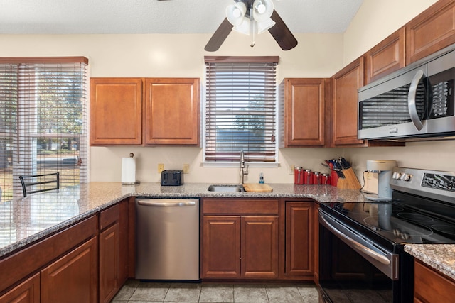 kitchen featuring ceiling fan, sink, stainless steel appliances, light stone counters, and a textured ceiling