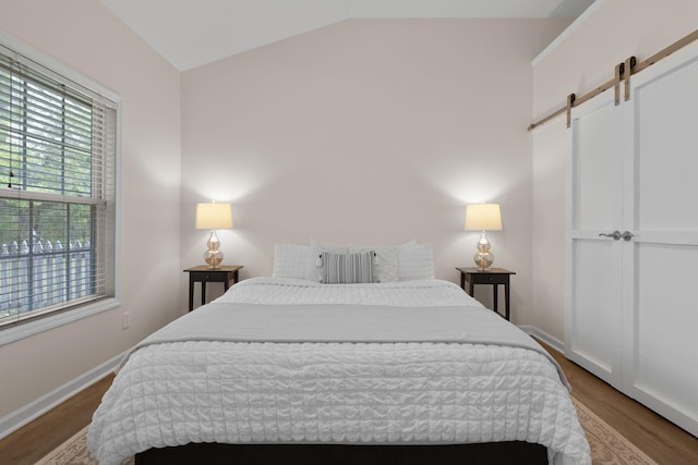 bedroom featuring multiple windows, vaulted ceiling, a barn door, and wood finished floors