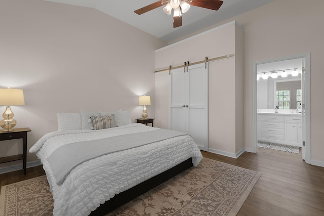 bedroom with baseboards, a barn door, lofted ceiling, and wood finished floors