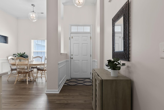 foyer featuring visible vents, ornamental molding, wainscoting, a decorative wall, and dark wood-type flooring
