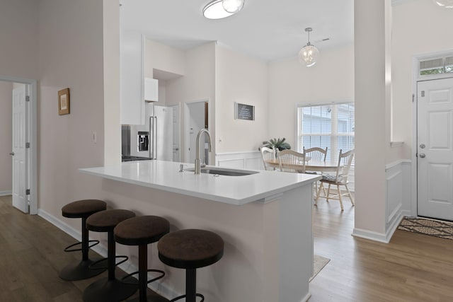 kitchen with a kitchen bar, stainless steel refrigerator with ice dispenser, wood finished floors, a sink, and white cabinets