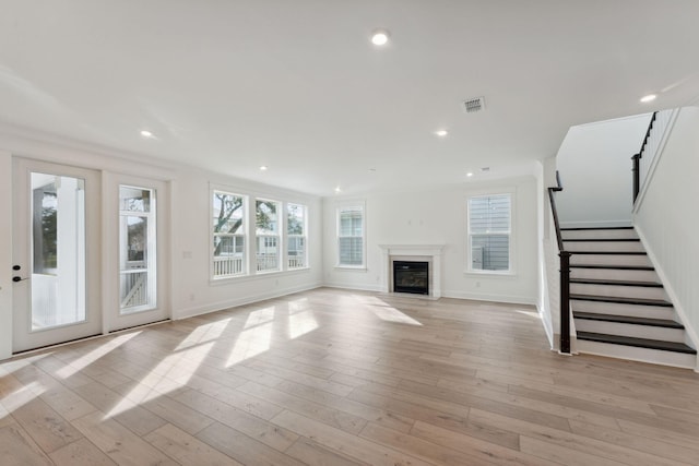 unfurnished living room with visible vents, light wood-style flooring, recessed lighting, stairs, and a glass covered fireplace