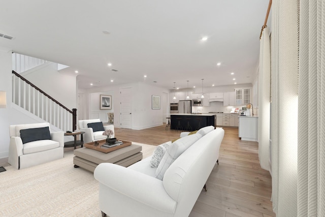 living area with recessed lighting, light wood-style flooring, stairs, and baseboards