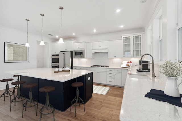 kitchen with a sink, a kitchen breakfast bar, backsplash, appliances with stainless steel finishes, and crown molding