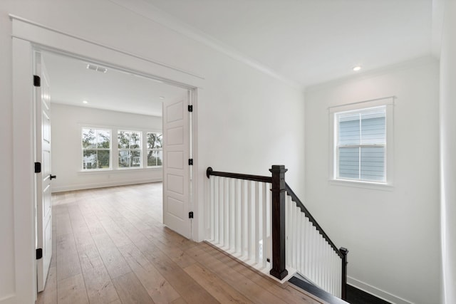 hallway with an upstairs landing, baseboards, light wood finished floors, and ornamental molding