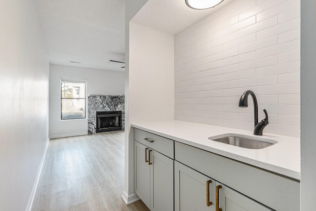 kitchen with gray cabinetry, sink, light wood-type flooring, a textured ceiling, and a premium fireplace