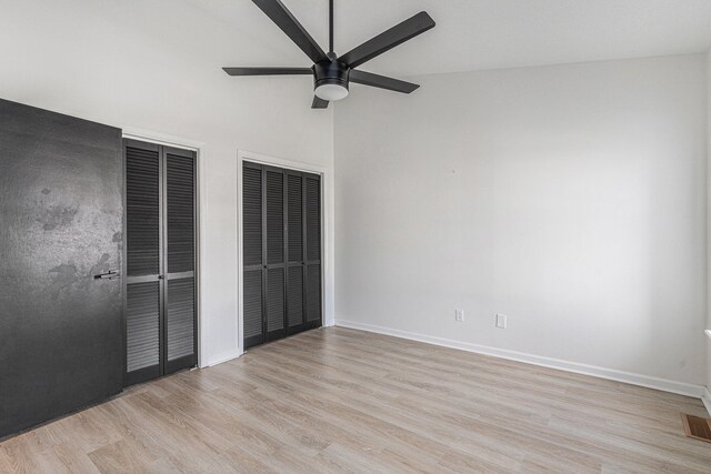 unfurnished bedroom featuring multiple closets, ceiling fan, light hardwood / wood-style floors, and lofted ceiling