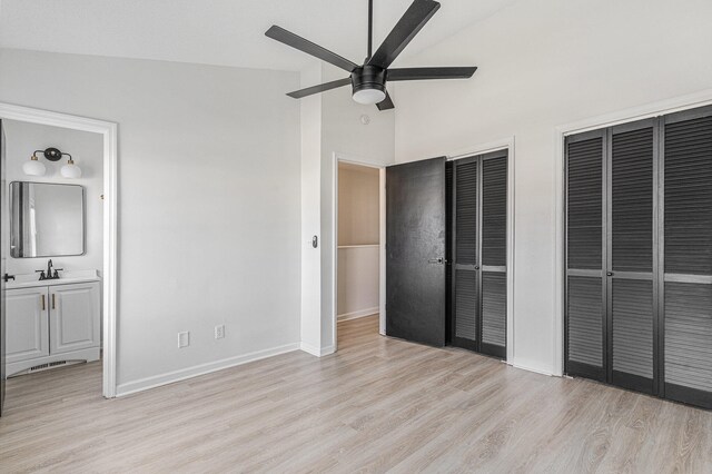 unfurnished bedroom with ensuite bathroom, vaulted ceiling, light hardwood / wood-style flooring, ceiling fan, and multiple closets