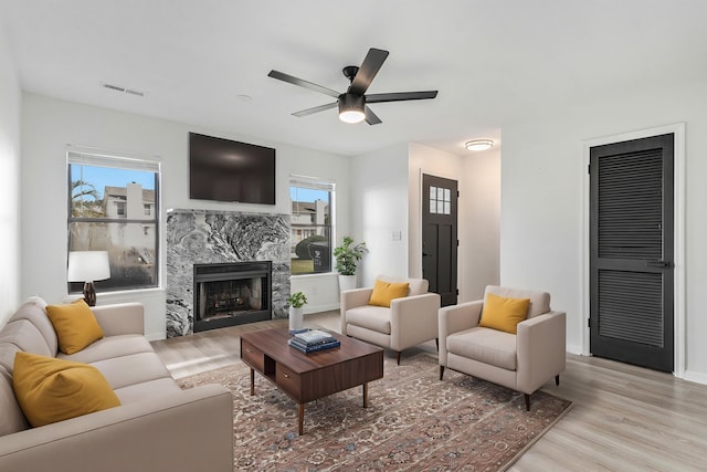 living room featuring a premium fireplace, plenty of natural light, ceiling fan, and light hardwood / wood-style floors