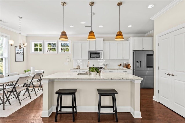 kitchen with appliances with stainless steel finishes, a chandelier, a breakfast bar, white cabinetry, and ornamental molding