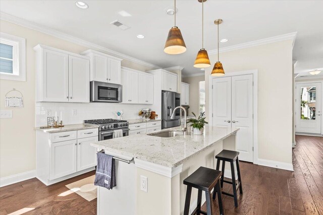 kitchen featuring appliances with stainless steel finishes, a kitchen island with sink, a sink, decorative backsplash, and a kitchen bar