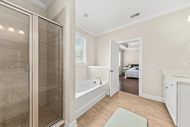 ensuite bathroom featuring ornamental molding, a stall shower, vanity, a garden tub, and baseboards