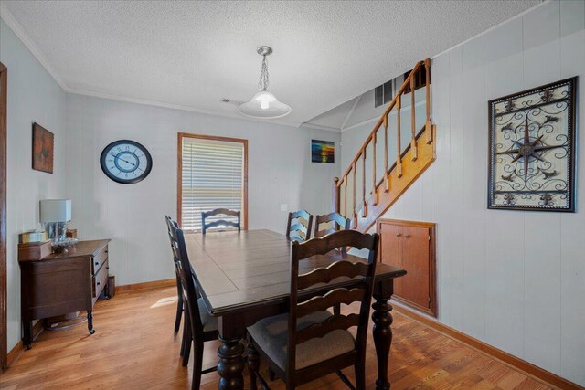 dining area featuring light wood-style flooring, a textured ceiling, stairs, and baseboards