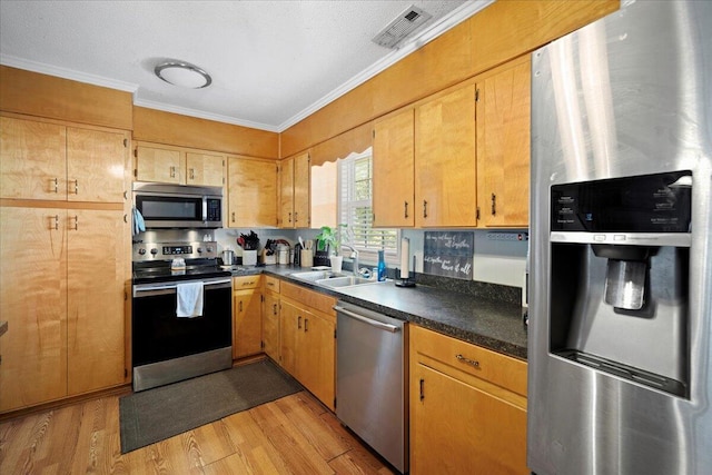 kitchen with visible vents, crown molding, light wood-style flooring, stainless steel appliances, and a sink