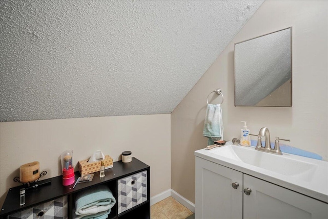 bathroom with vanity, vaulted ceiling, baseboards, and a textured ceiling