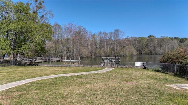 view of yard featuring a water view, fence, a boat dock, and a wooded view