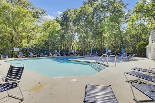 community pool with fence, a patio area, and view of scattered trees