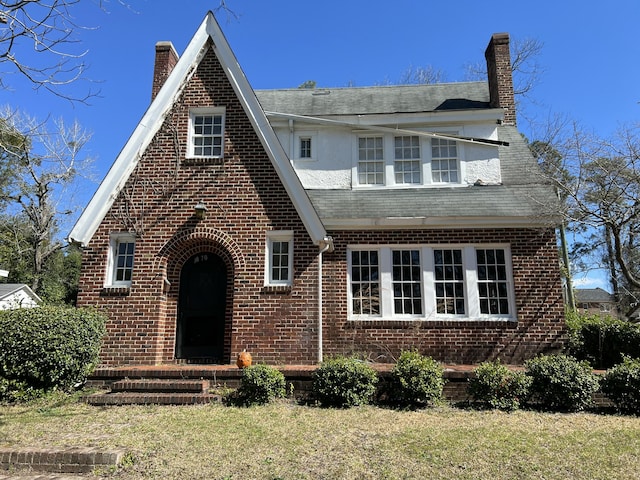 english style home featuring brick siding, a chimney, and a front yard