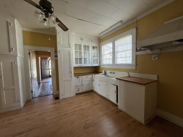 kitchen with glass insert cabinets, light wood-style floors, white cabinetry, a ceiling fan, and a sink