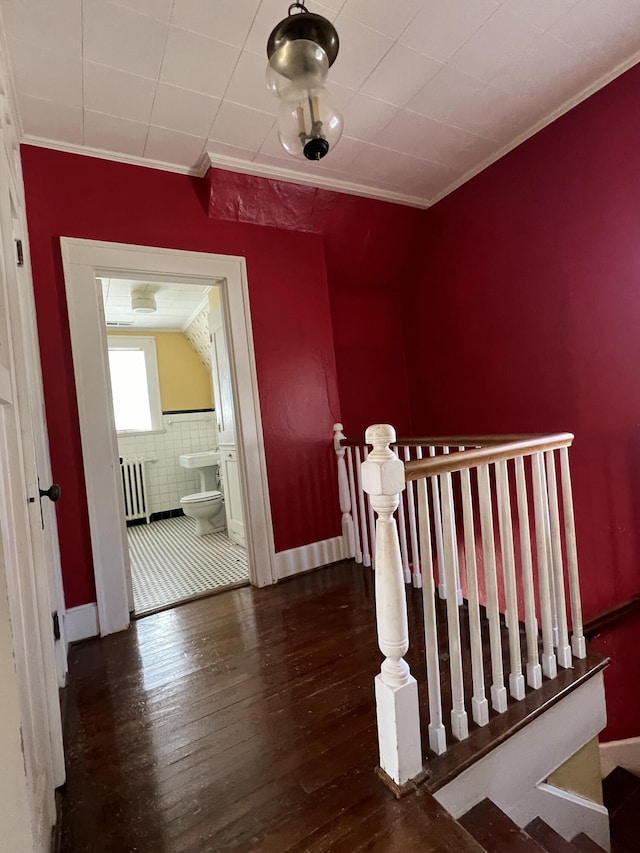 staircase with radiator heating unit, wood finished floors, and ornamental molding