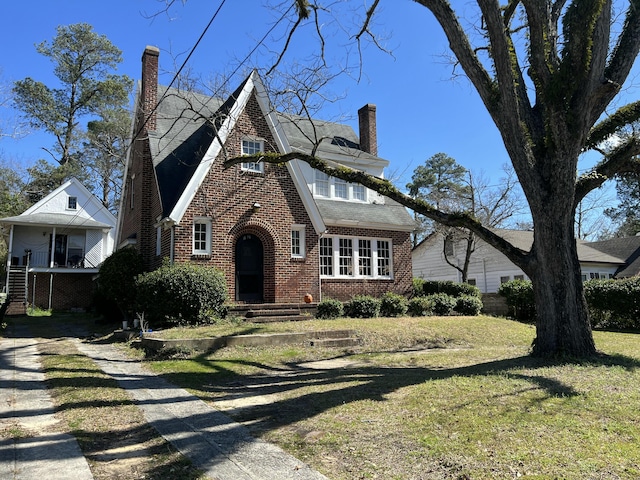 tudor house with a front yard, brick siding, and a chimney