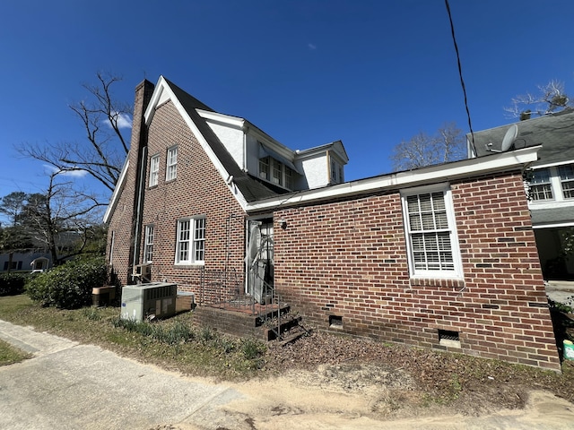 rear view of house with brick siding, central AC, and a chimney