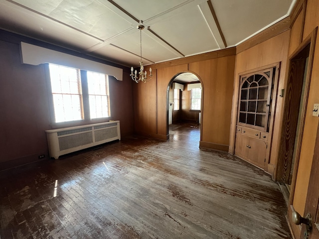 unfurnished dining area featuring arched walkways, a healthy amount of sunlight, radiator heating unit, and wood finished floors