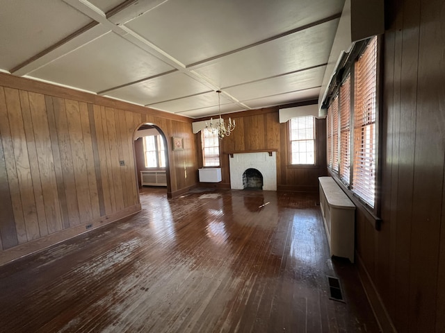 unfurnished living room with radiator, visible vents, dark wood finished floors, a fireplace, and a chandelier