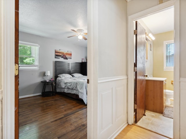 bedroom with ceiling fan, a textured ceiling, hardwood / wood-style flooring, and connected bathroom