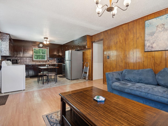 living room with light hardwood / wood-style floors, washer / clothes dryer, a textured ceiling, ceiling fan with notable chandelier, and wood walls