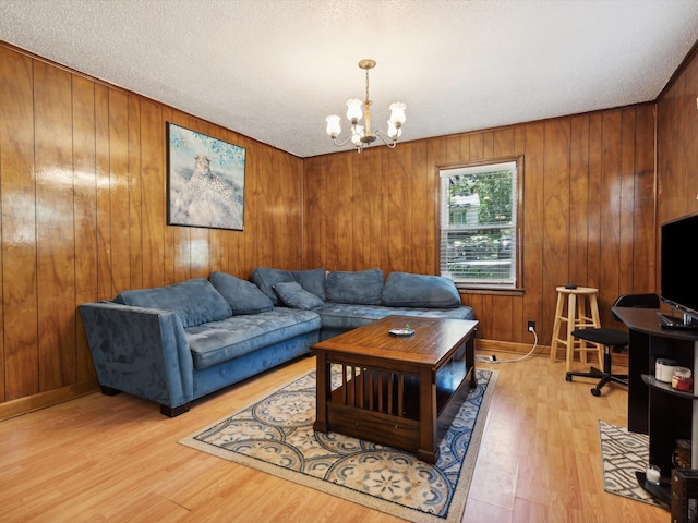 living room with a notable chandelier, light hardwood / wood-style flooring, a textured ceiling, and wooden walls