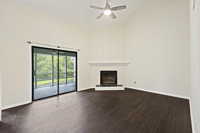 unfurnished living room with a fireplace with raised hearth, a towering ceiling, ceiling fan, wood finished floors, and baseboards