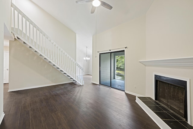 unfurnished living room featuring baseboards, a tile fireplace, dark wood-style flooring, a high ceiling, and ceiling fan with notable chandelier