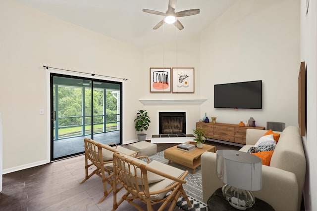 living area with baseboards, a fireplace with raised hearth, dark wood finished floors, a ceiling fan, and high vaulted ceiling