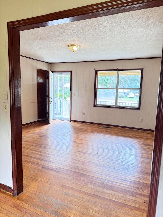 unfurnished room featuring light wood-type flooring, wooden walls, and a textured ceiling