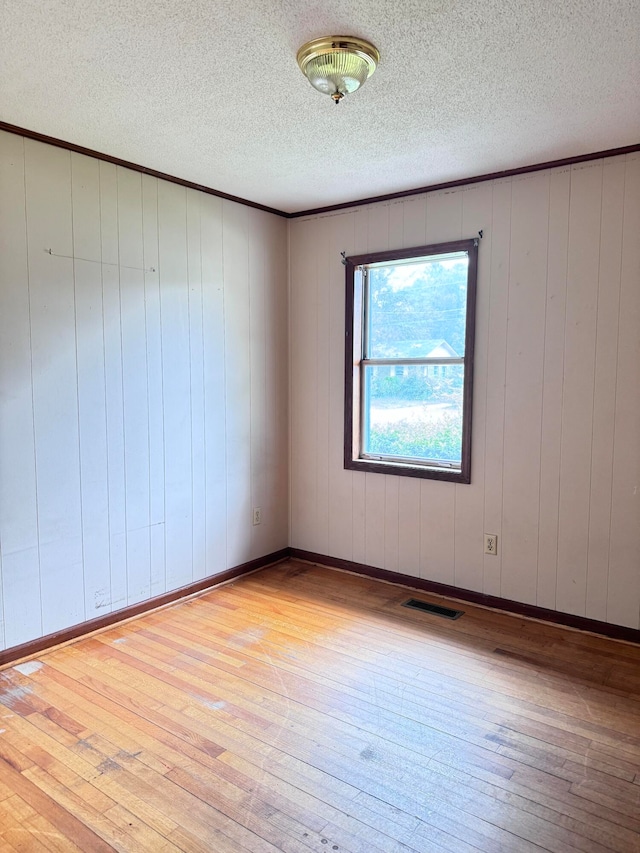 unfurnished room featuring light wood-type flooring, a textured ceiling, and wood walls