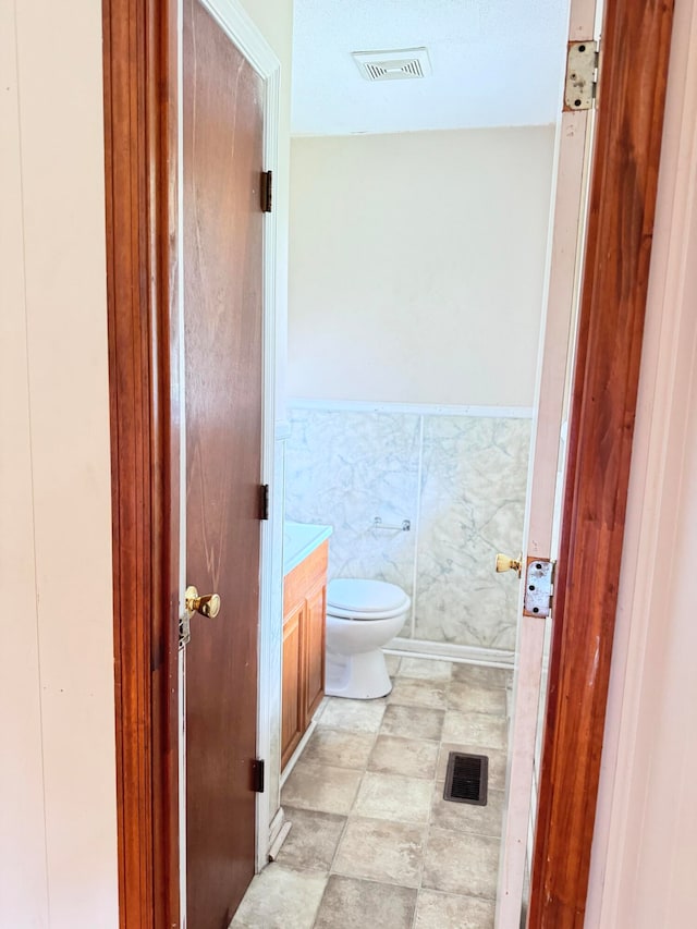 bathroom featuring vanity, toilet, and tile walls